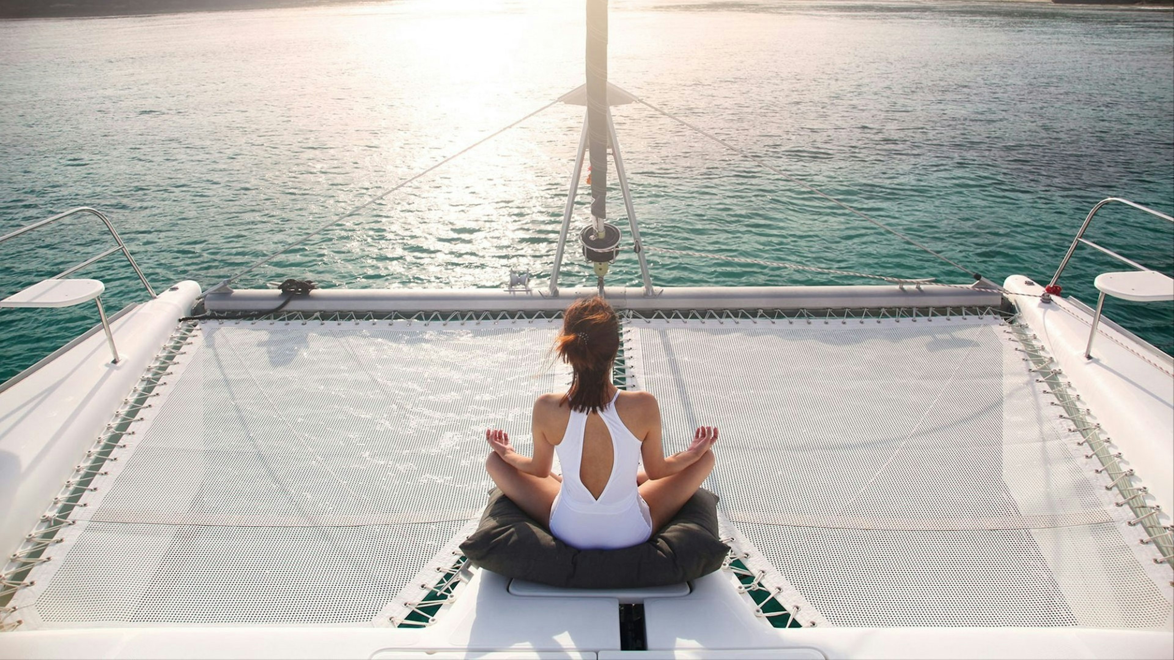 Woman wearing white swimsuit. Meditation on a catamaran sailboat