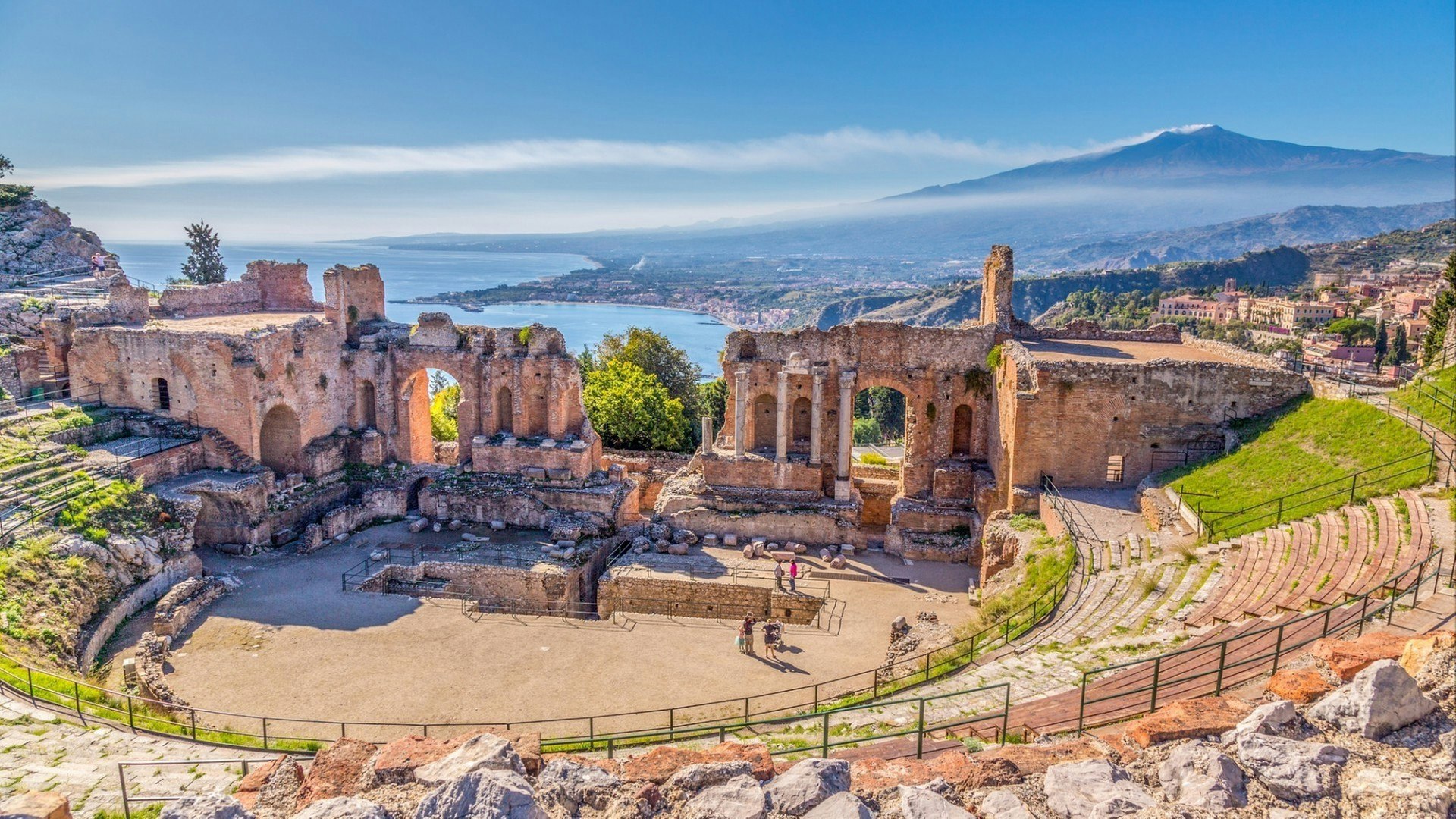 Ruins of the Ancient Greek Theater in Taormina, Sicily with the double smoke tail of the Etna extending over the the Giardini-Naxos bay