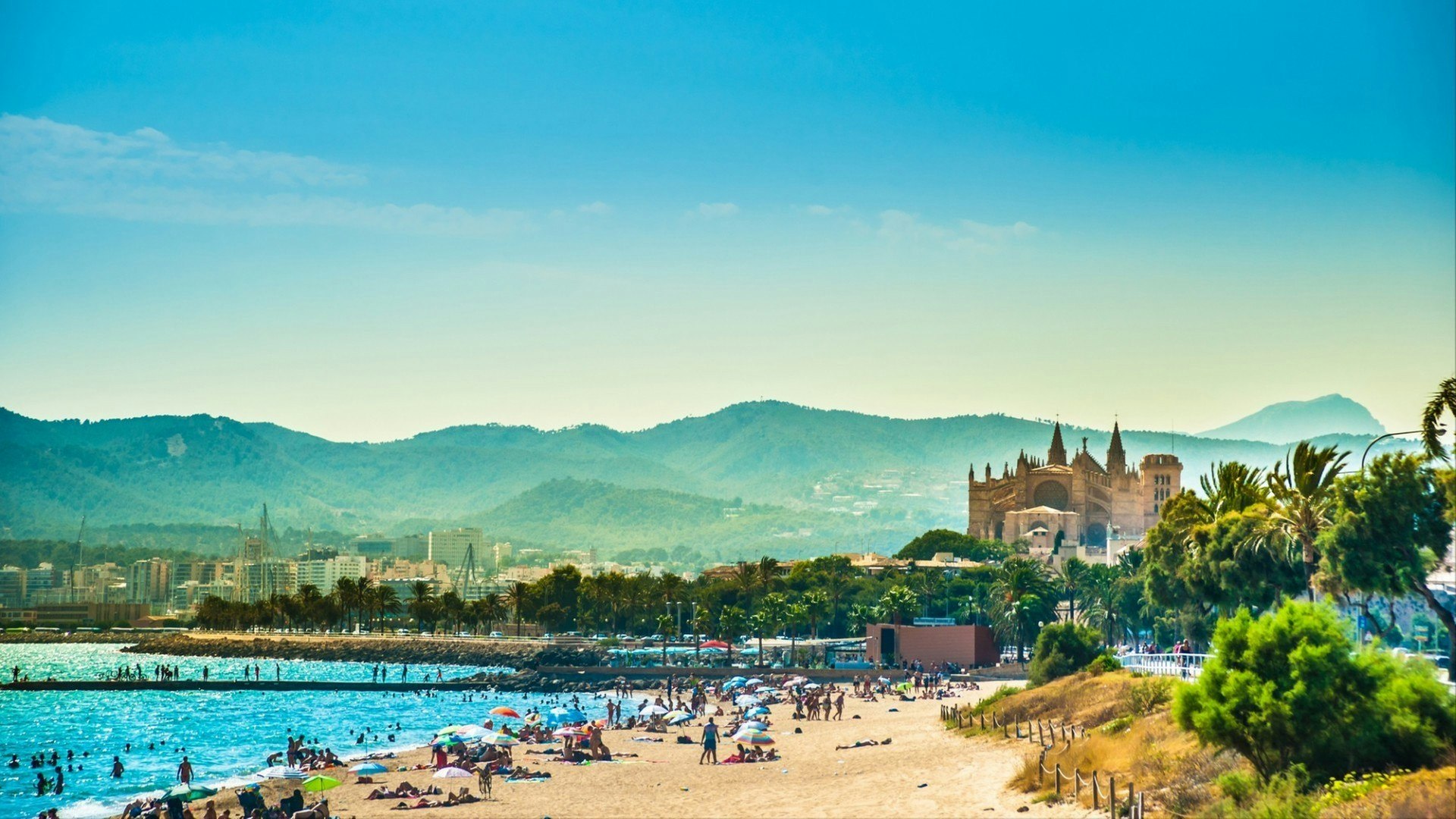 View of the beach of Palma de Mallorca with people lying on sand and the gorgeous cathedral building visible in background